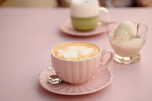 Appetizing cappuccino in a pink cup on a pink table close-up. Next to it are vanilla ice cream and matcha latte.
