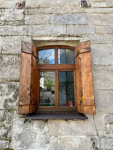 Brown wooden window with open shutters on a stone medieval wall.
