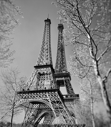 A vintage looking skyline photo taken in Paris France. The Eiffel Tower is to the right of the frame with dramatic clouds in the sky as a background.