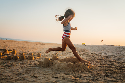 Playful little girl running and jumping on the shore of the beautiful beach in Algarve Portugal
