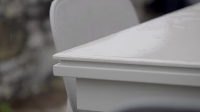 Raindrops falling on plastic garden patio furniture close up Slow motion