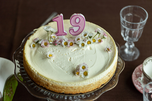 Cheesecake with live daisy flowers on a decorative stand with the number 19