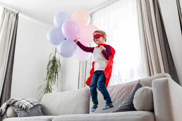 istock Child Superhero with Balloons Jumping on Sofa 2148884425