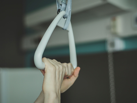 Caucasian male patient holds with both hands a triangular therapeutic archwire with a gripper set above the bed in a hospital room, close-up side view. The concept of trauma devices.