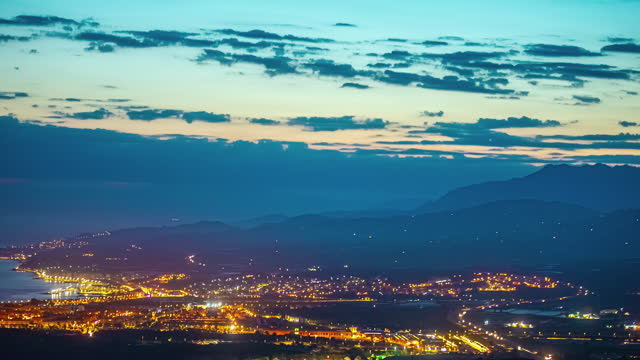 Orange golden hour sky recedes to dusk glow as Malaga Spain city lights up at night