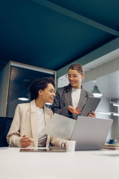 istock Two smiling business woman work together with documents and use digital tablet at the office 2148887807
