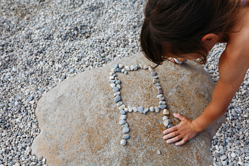 close up view on child arm and hand making letter A on big stone on the beach