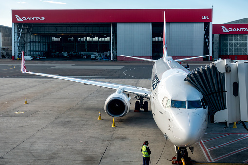 Sydney, Australia - Aug 28, 2022: Qantas airplane docked onto a jetway at Sydney Domestic Airport. Ground crews arriving for maintenance.