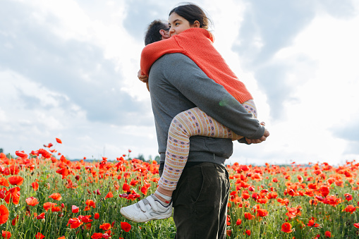 low angle view of father holding daughter in the arms on a sunny day standing in the big field of poppies