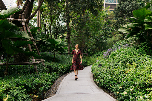 Full length shot of young woman walking alone in the park. Beautiful woman in casuals walking on small road in park.
