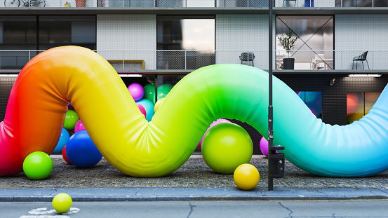 A surreal scene of multi colored inflatable objects on the city street.