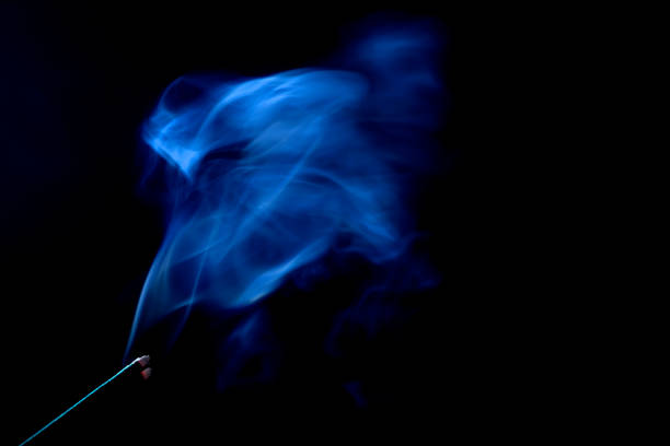 A single match ignites, casting a warm glow and ethereal smoke against a dark backdrop. Fire, smoke, and sparks dance in the darkness.