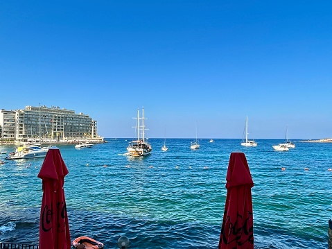 view of a bay of Malta between two closed red umbrellas and boats on the Mediterranean on a sunny summer day