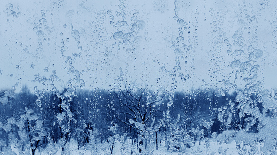 Frozen rain drops on a window with a blurry snowy view. Drops of ice and rain on a window overlooking a winter blue snowy forest.