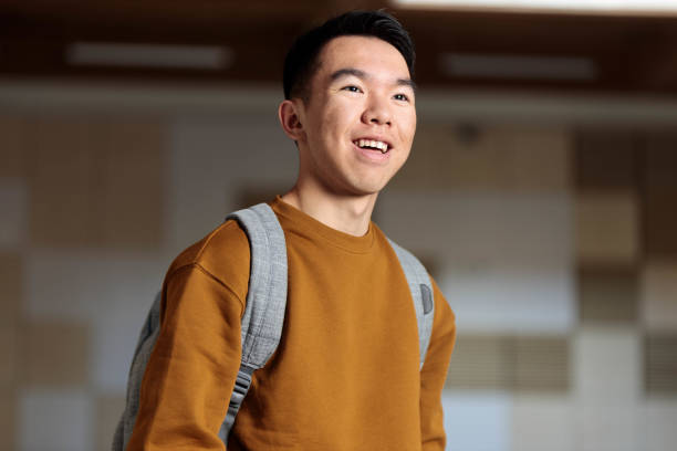 istock A young student in a brown sweater and backpack happily standing in a classroom 2148896560