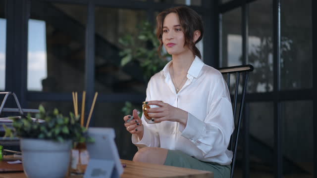 An unrecognizable female secretary brings a cup of coffee to a businesswoman sitting at a table in office. The woman thanks for the coffee and gives the secretary the signed documents.