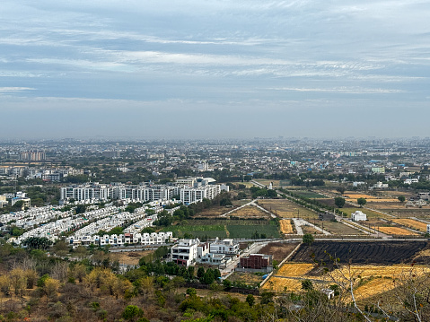 A city with a mountain in the background, at Ralamandal, Indore, India. The sky is cloudy and the city is mostly white