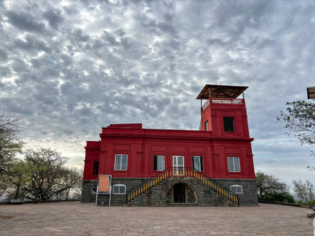 A red building with a sign on the front at Ralamandal, Indore, India. The building is surrounded by trees and has a large staircase leading up to it.