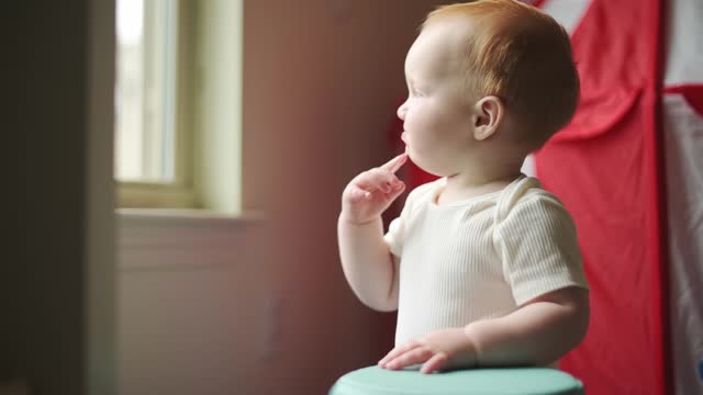 one year old boy plays in the child's room with a roller, exploring the environment with a finger in the mouth