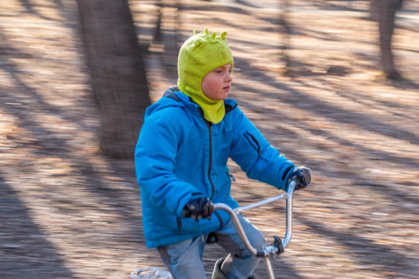 Seven years old little boy rides a bicycle in the autumn park. A boy in a blue jacket and yellow hat is cycling through a park