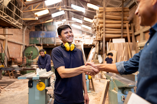 Latin American foreman handshaking a new employee at a wood factory and smiling