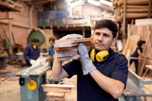 Latin American man working at a timber factory carrying planks of wood