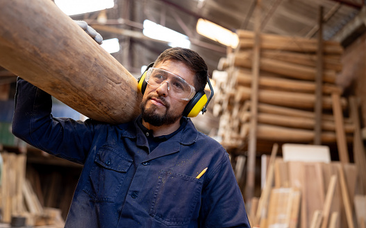 Latin American man working at a timber factory carrying a log of wood