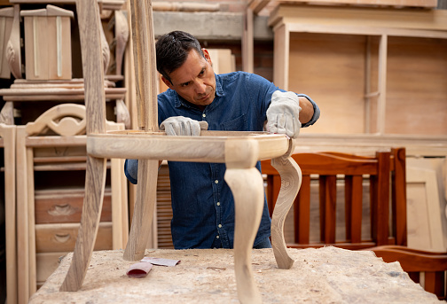 Latin American carpenter working at a furniture factory sanding a chair