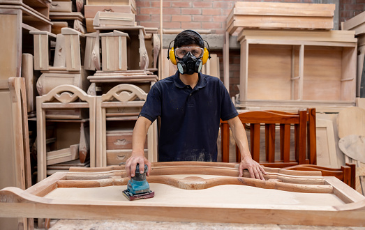 Portrait of a Latin American worker sanding wood at a timber factory and wearing a gas mask