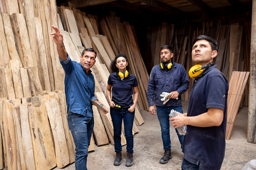 Foreman giving instructions to a group of workers in a staff meeting at a timber factory