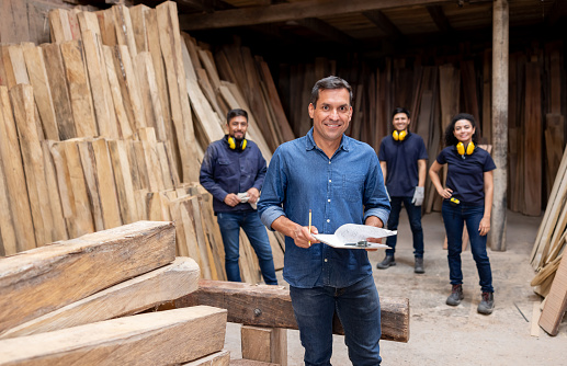 Latin American business manager working with a group of workers at a lumberyard and looking at the camera smiling