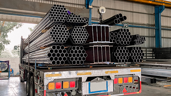 Trucks with long trailers carry rebar for building construction. Construction steel ready to be delivered to customers, steel transport vehicles, black steel pipes, structural steel.