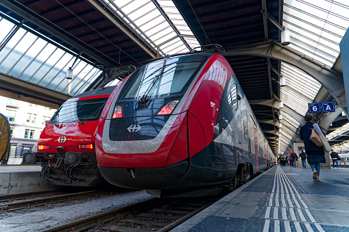 Diminishing perspective of red trains at Zürich main railway station on a sunny spring morning with passengers on platform at Swiss City of Zürich. Photo taken April 11th, 2024, Zurich, Switzerland.