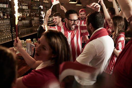 Cheerful soccer fans screaming of joy in a bar after their favorite team has won the game.
