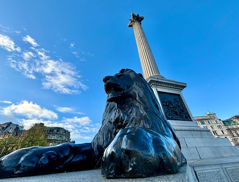 Bronze Lion at Trafalger Square with Union Jack flags flying in the background.