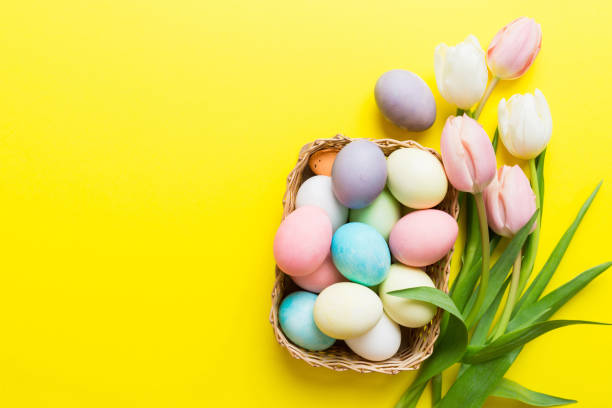 istock Happy Easter composition. Easter eggs in basket on colored table with yellow Tulips. Natural dyed colorful eggs background top view with copy space 2148925951
