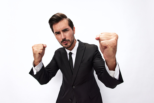 Portrait of a man in an expensive business suit close-up wide-angle lens pulling his hands to fight into the camera with his mouth open screaming his fists up on a white background, copy space. High quality photo