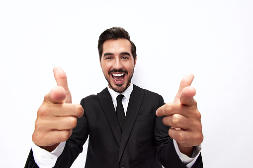 Portrait of a man in an expensive business suit close-up wide-angle lens pulls his hands into the camera with his mouth open and points his thumb up against a white background, copy space. High quality photo
