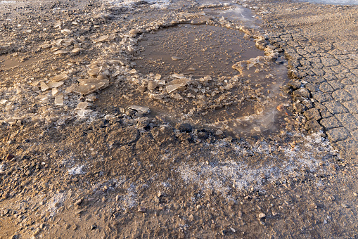 a badly damaged road in ice in winter, a large number of holes and dirt on the highway in winter