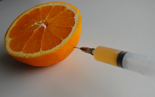 Vitamins content in fruits illustration. Orange juice fills a syringe, the needle of which is inserted into the half of the juicy orange through the peel