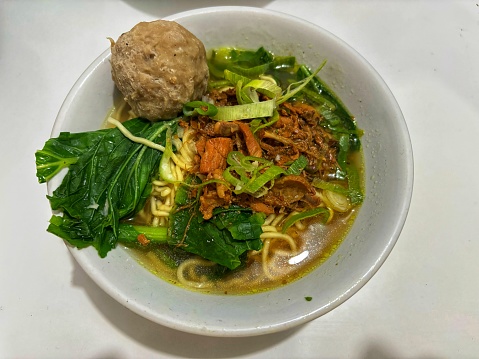 A bowl of bakso chicken noodle soup, with a generous meatball, tender greens, and crispy shallots