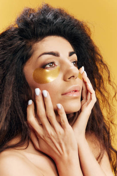 istock Attractive Latin lady in gold hydrogel patches under eye touch cheek look aside posing isolated over yellow background. Cosmetic product ad Natural beauty Skincare concept Anti wrinkle procedure 2148928552