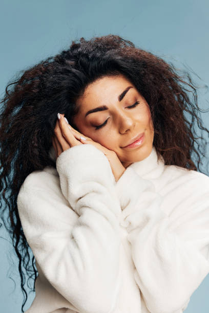 istock SPA PROCEDURE CONCEPT. Smiling happy curly Latin lady enjoy soft bathrobe touching face, recline on hands, sleeping, posing isolated on pastel blue background, closing eyes. Copy space, beauty banner 2148930126