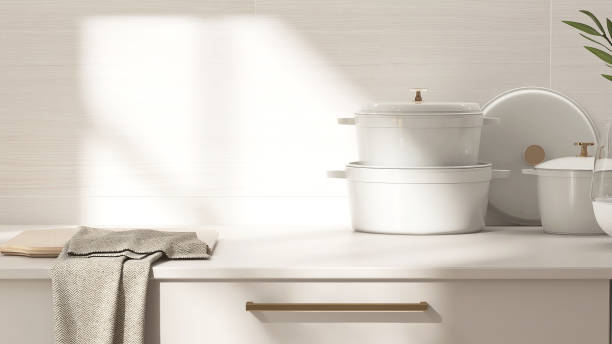 Beige kitchen table counter, cutting board, pots on countertop in sunlight on wood pattern tile wall in background