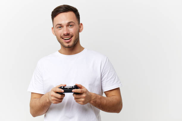 istock Smiling cheerful tanned handsome man in basic t-shirt enjoy cool game with joystick gamepad posing isolated on over white studio background. Copy space Banner Mockup. Gamer RPG concept 2148931502