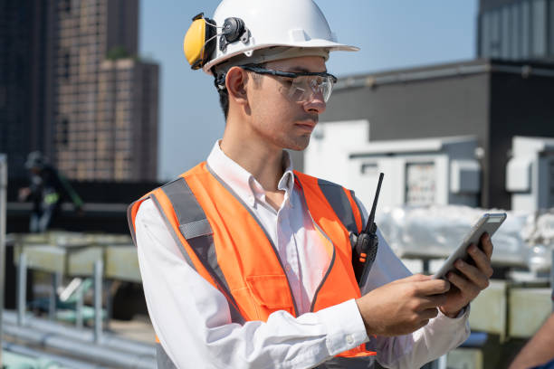 istock Portrait Asia male engineer in protective workwear is performing a conducts system check with use paperwork and walkie talkie at rooftop building 2148931630