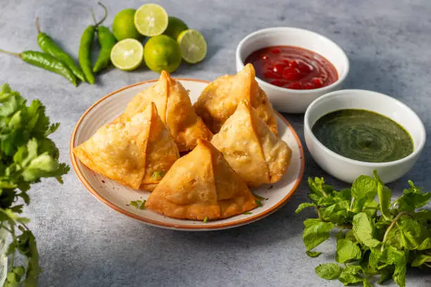 Photo of selective focus Samosa, Spiced potato-filled pastry, crispy, Savory, popular Indian snack with tomato and mint chutney.