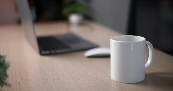 Selective focus ,Cup of coffee laying on a desk beside a laptop in home office with no people there, Home workspace