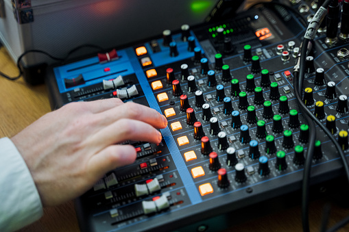 A sound engineer is using a mixing console with various knobs to adjust audio levels for an event. This electronic device is essential in the world of entertainment and engineering