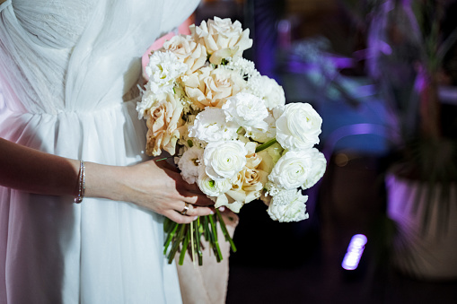 The bride gracefully holds a bouquet of white roses, a timeless gesture symbolizing love and purity, complementing her elegant white wedding dress